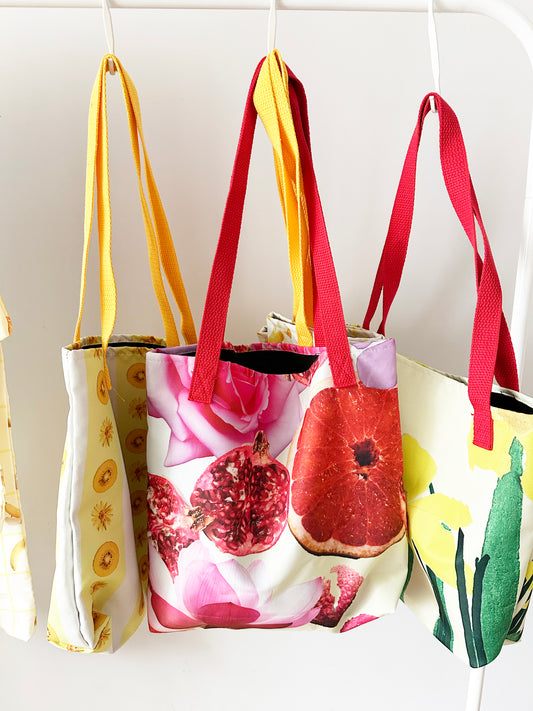 Three colourful tote bags with floral, pomegranate, and nature-themed designs on a white background.