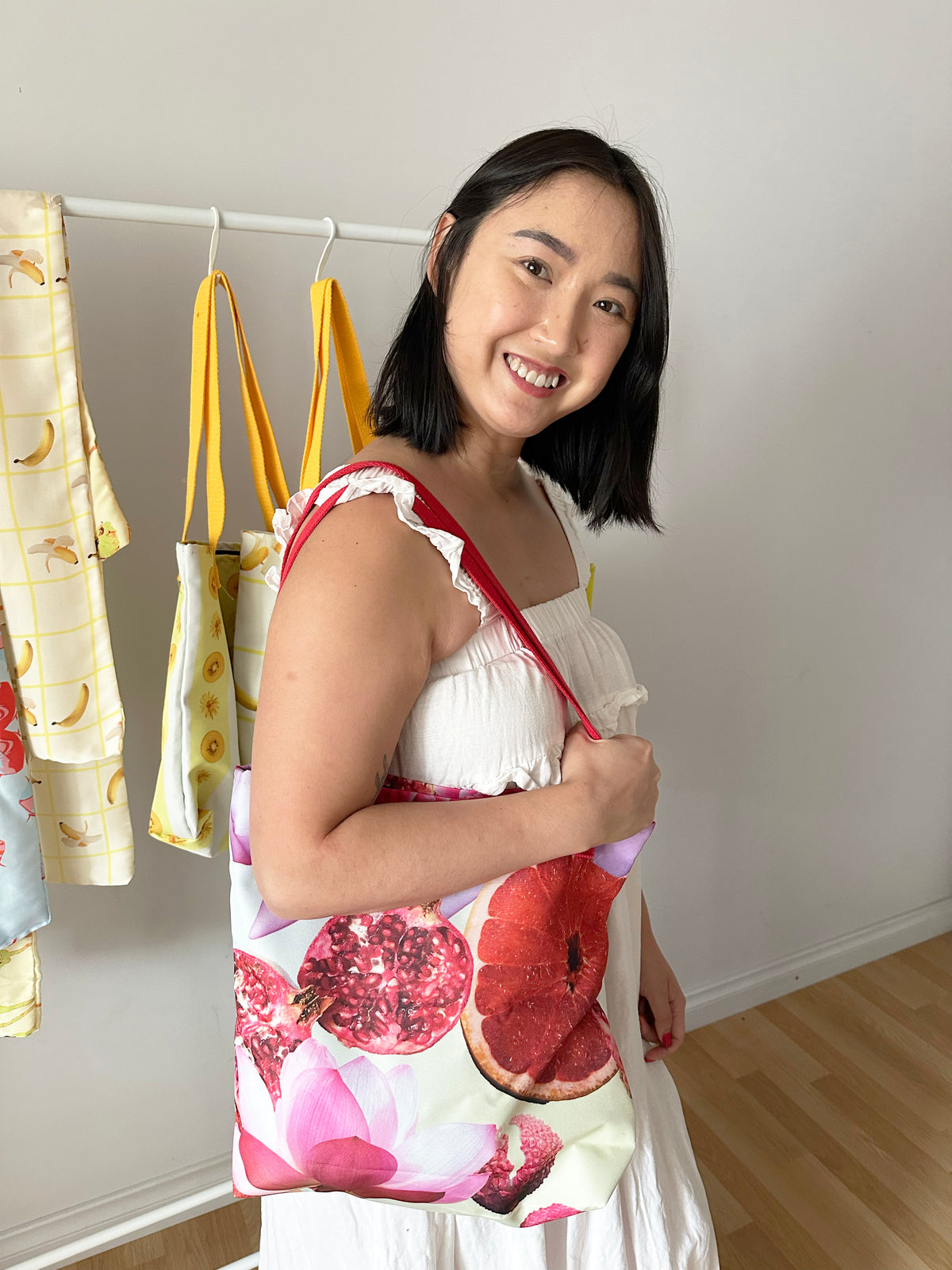 Woman holding a tote bag with pomegranate design in a room with hanging Duyen Del Design products.