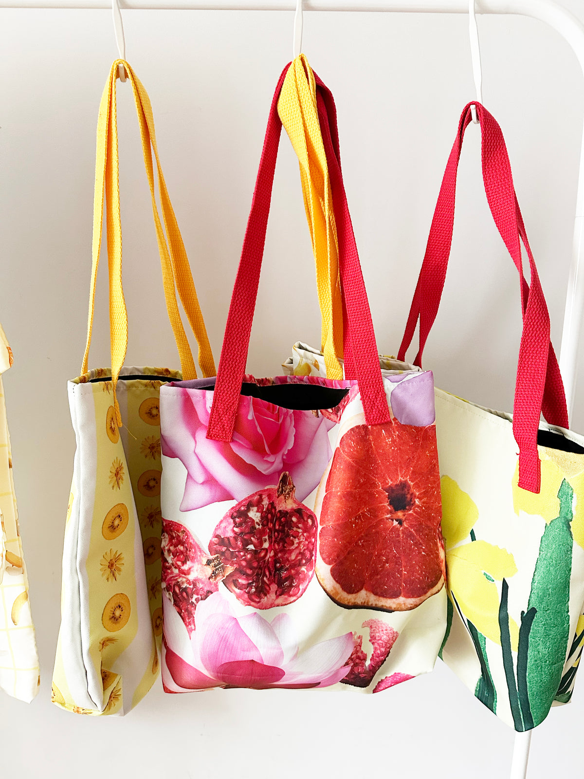 Three colourful tote bags with floral, pomegranate, and nature-themed designs on a white background.